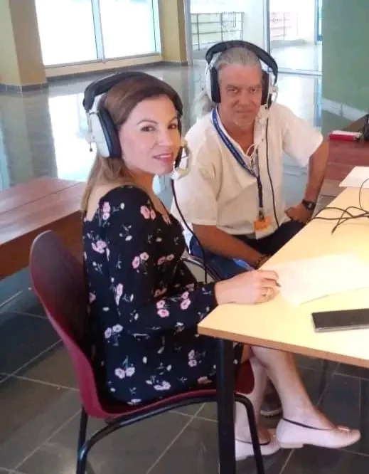 Two people wearing headphones at the microphones in a radio booth