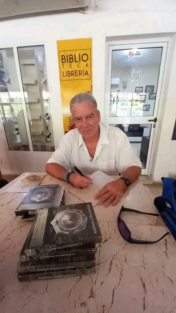 Firma de ejemplares sentado a una mesa, ante la puerta de una librería