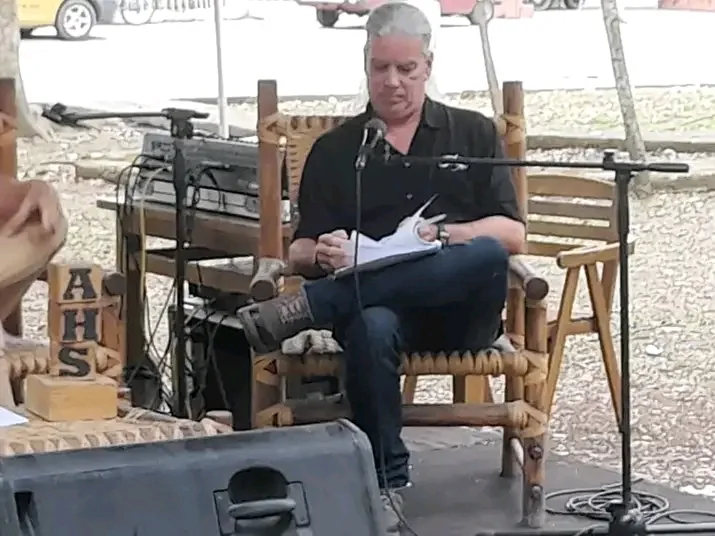 Lectura de poemas al aire libre, sentado ante un micrófono