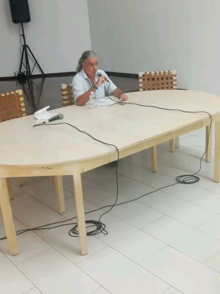 Intervención ante el micrófono en una mesa larga durante un evento teórico
