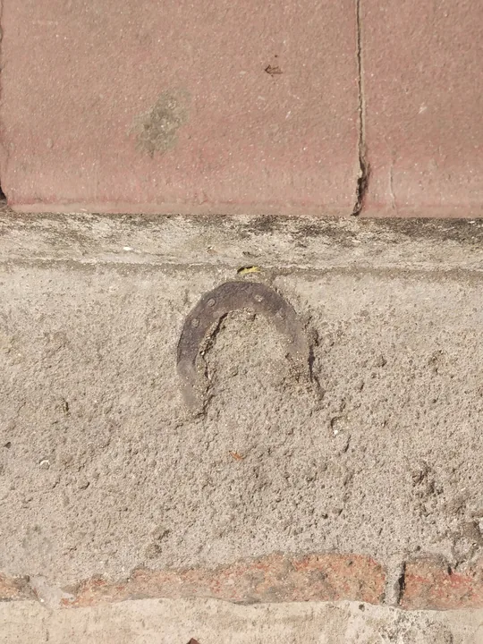 Una herradura vieja incrustada en el cemento de un escalón, bajo una hilada de ladrillos rojos