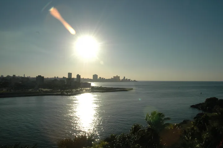 El sol bajo sobre la bahía, con el perfil de la ciudad al fondo y un reflejo encendido que parte el agua en dos