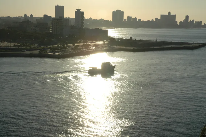 Un barco pequeño cruza el reflejo del sol en la bahía, con la ciudad a contraluz al fondo