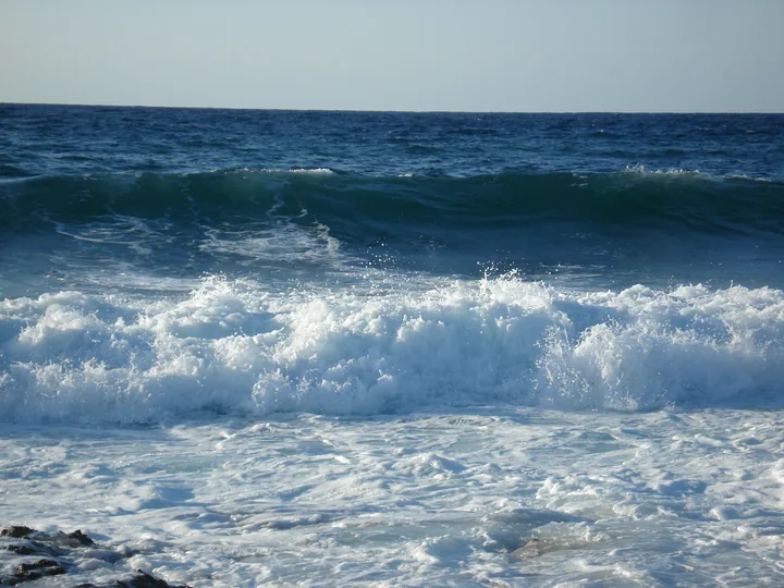 La mer bleue se brisant en vagues blanches contre des rochers, sous un ciel clair