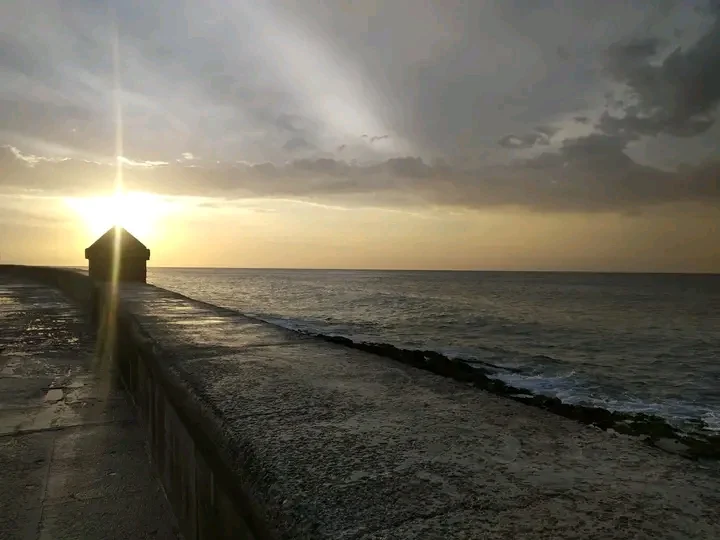 Atardecer sobre el muro del malecón, con el sol abriéndose paso entre las nubes
