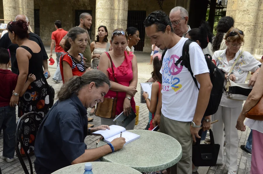 Signing copies at an open-air table, surrounded by readers
